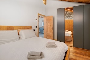 Ein Schlafzimmer mit einem hölzernen Kopfteil, einem Bett mit weißer Bettwäsche, einem Holzschrank und einer Tür zu einem anderen Raum.