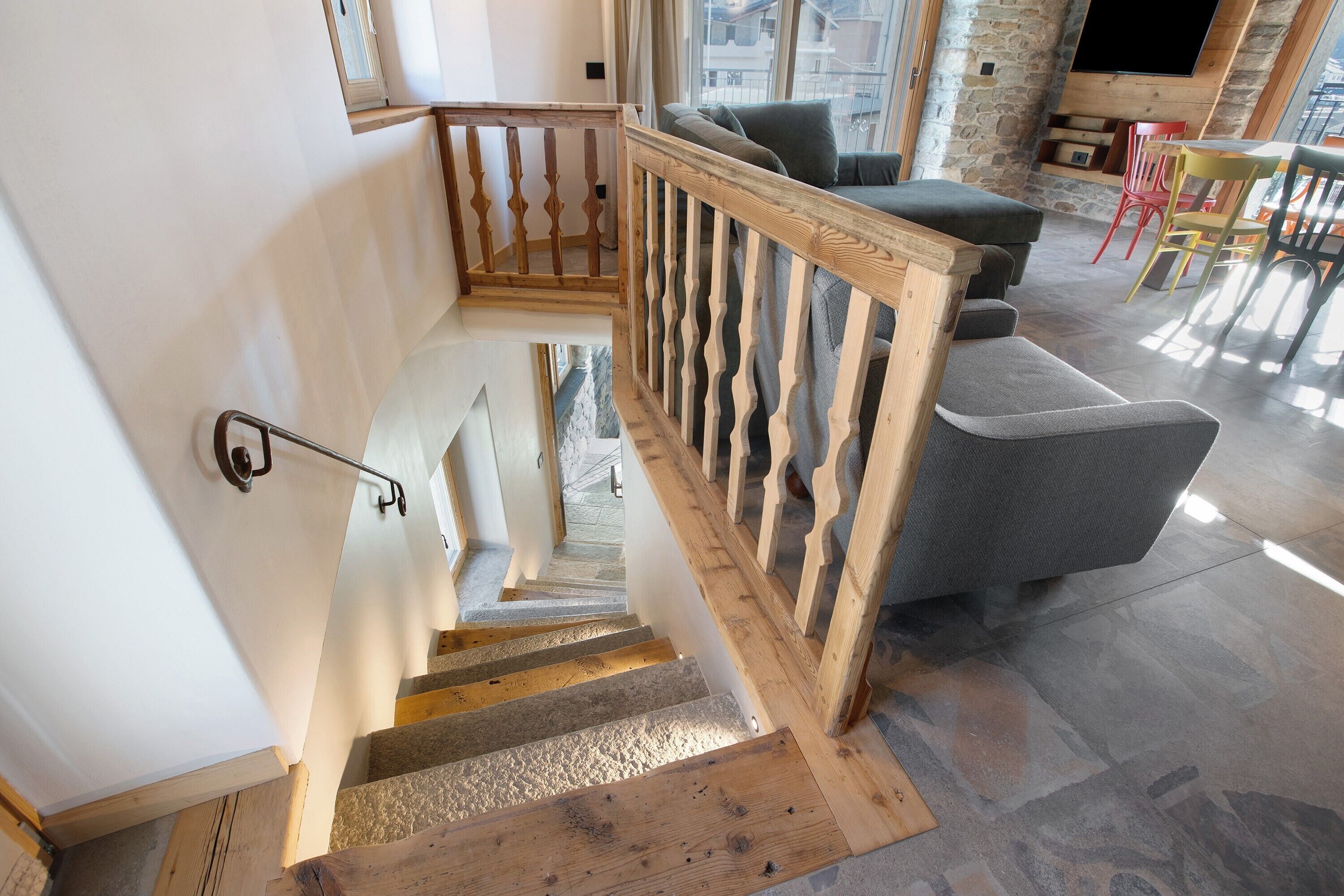 A staircase with wooden railings leading to a living area with a sofa and chairs.