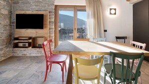 Une pièce avec un mur en pierre, un plafond en bois, une grande fenêtre donnant sur un beau paysage, un téléviseur à écran plat et une table à manger avec des chaises.