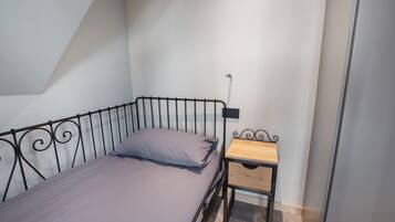 Un lit simple avec un cadre en métal, une table de chevet en bois avec un tiroir et un luminaire fixé au mur.