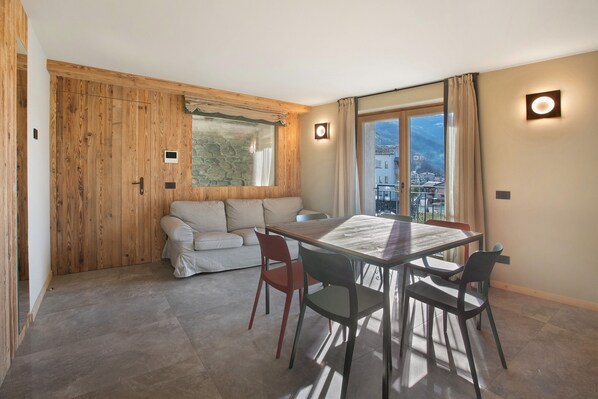 A room with a wooden partition, a sofa, a dining table with chairs, and a view through a window.