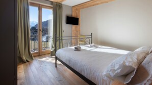 Un dormitorio con cama, televisor en la pared y balcón con cortinas.