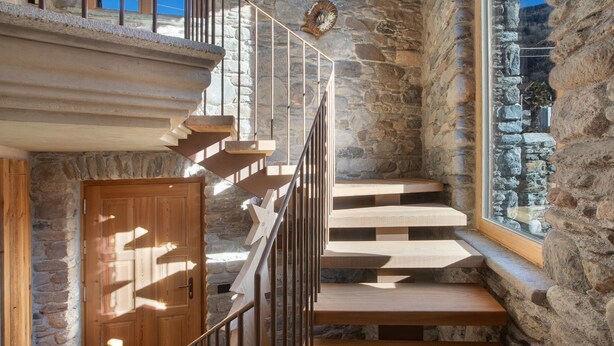 Una escalera de madera con barandillas metálicas que conduce a un muro de piedra con una ventana.