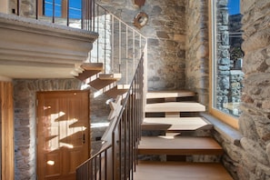 A staircase with wooden steps and metal railings, leading to a stone wall with a window.