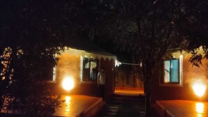 A night scene of a building with two illuminated rooms, a central staircase, and surrounding foliage. - Kross Adventure Campsite (Bali)