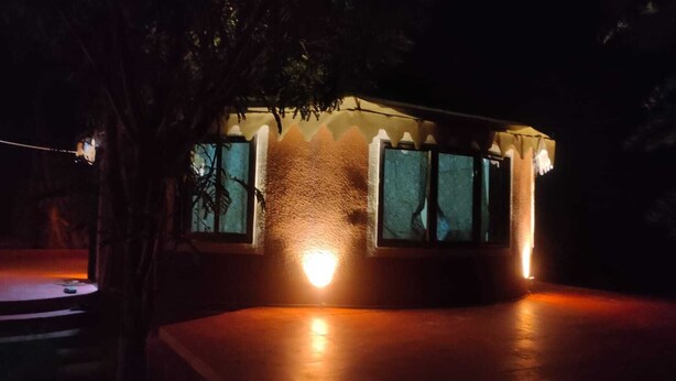 A building with a curved roof and two illuminated windows, surrounded by trees. - Kross Adventure Campsite (Bali)