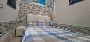 A bedroom with a checkered bedspread, a tufted headboard, a cushioned bench, and a stone-patterned wall. - Apartment 'Centro Di Alcamo' with Balcony, Wi-Fi and Air Conditioning (Alcamo)
