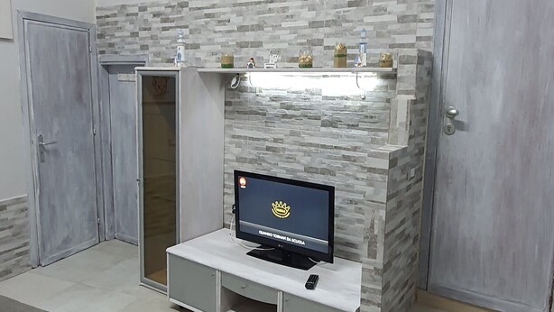 Una habitación de hotel con una televisión sobre un mueble blanco, un sofá gris y un armario.