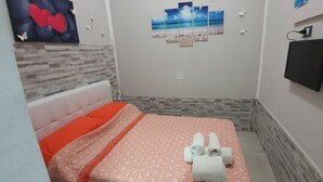 Habitación de hotel con cama, televisor de pared y una obra de arte que representa una escena de playa.