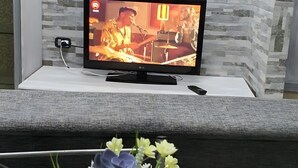 Un televisor sobre un pedestal blanco, un control remoto y un florero con flores sobre una mesa.