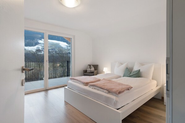 Une chambre moderne avec un grand lit, une table de chevet, une lampe et une vue sur un paysage enneigé, visible à travers une porte-fenêtre coulissante.