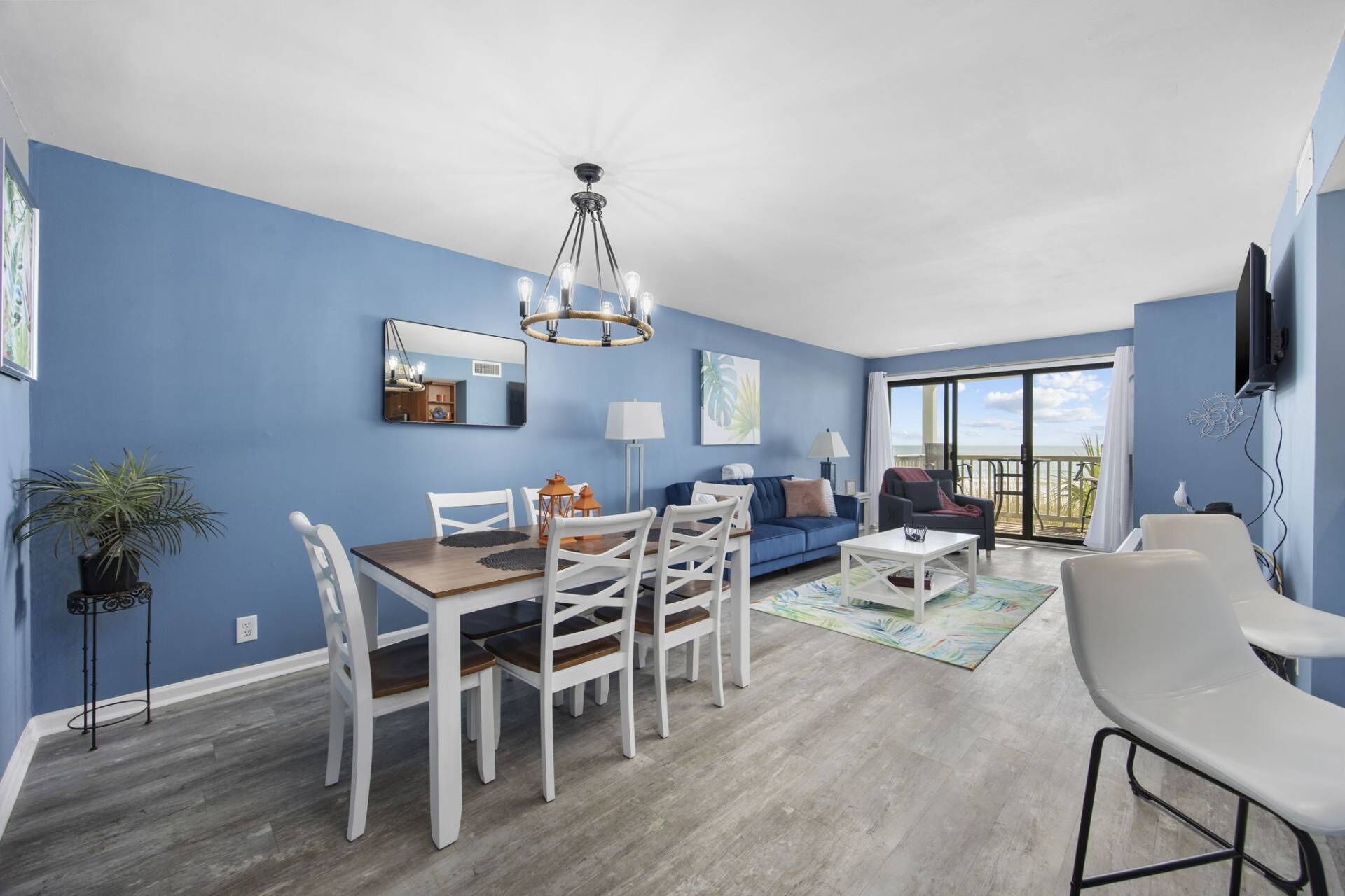 Un salon comprenant un coin repas, un mur bleu, un ventilateur de plafond et une vue sur l’océan grâce à de grandes fenêtres.