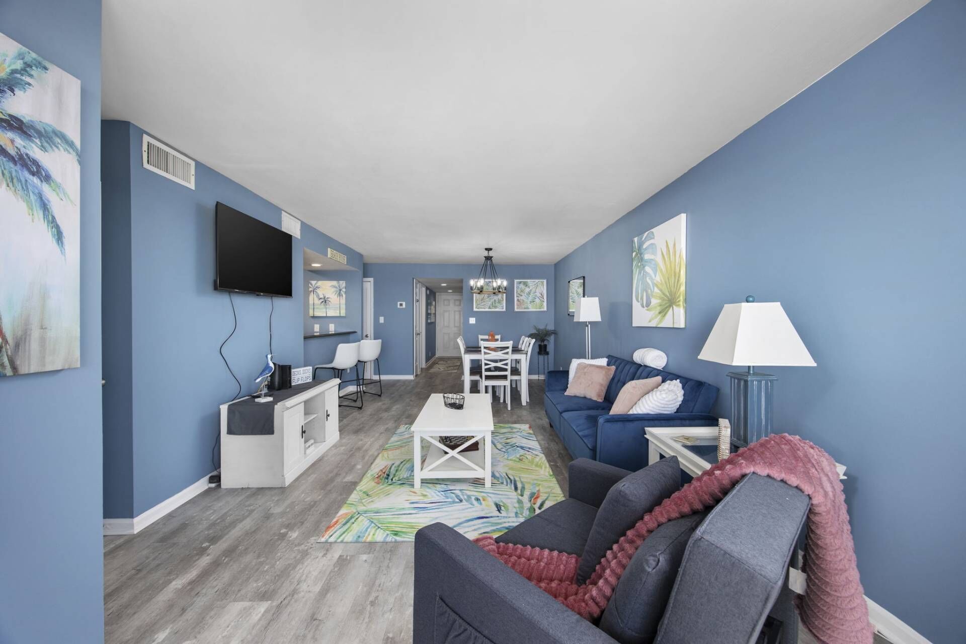 A living room with a blue wall, a TV, a desk, a couch, and a dining area.