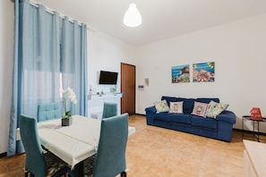Un salon avec un canapé bleu, une table à manger avec des chaises, un téléviseur et des œuvres d’art accrochées au mur.