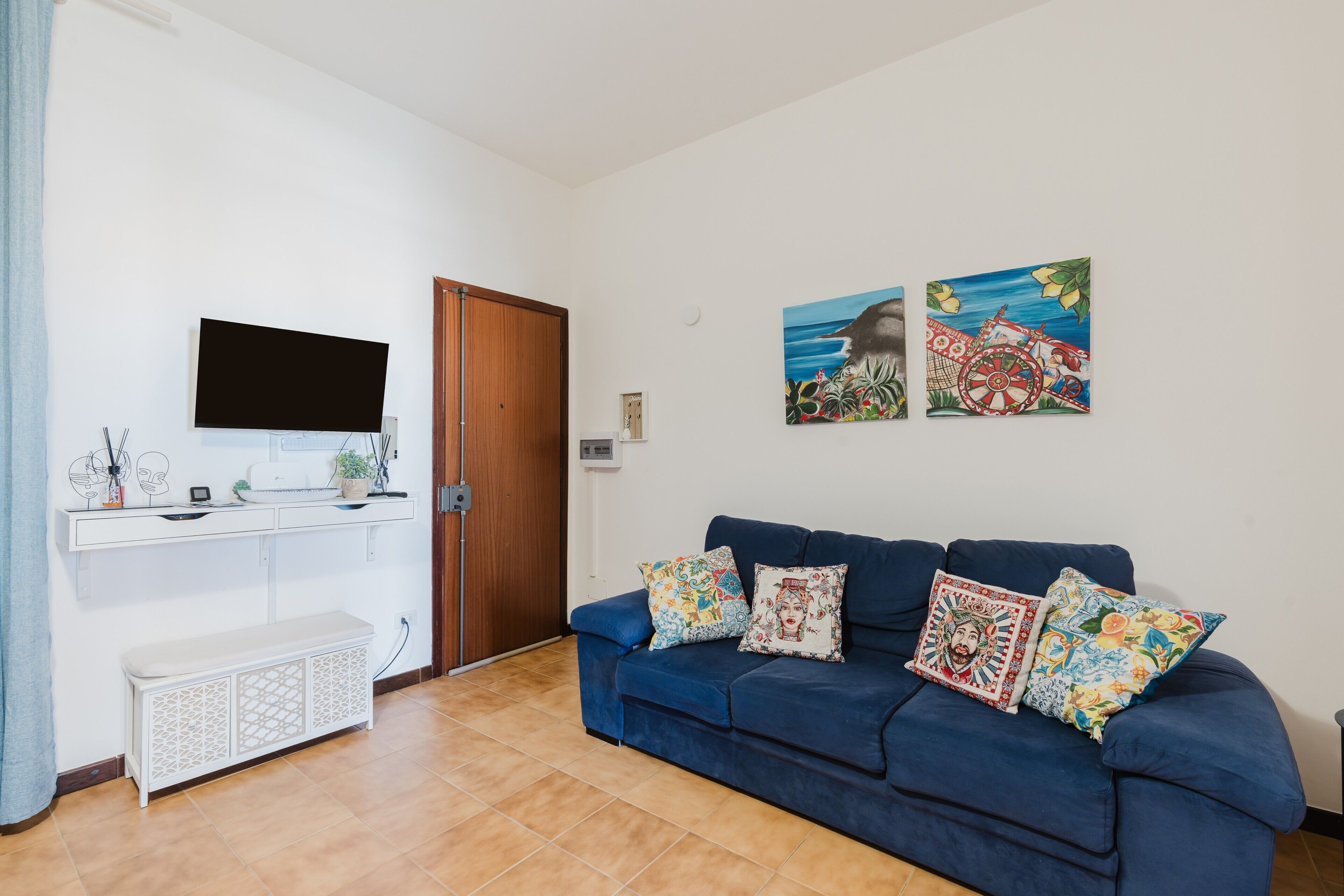 A living room with a blue sofa, a TV on a white stand, and two wall-mounted paintings.