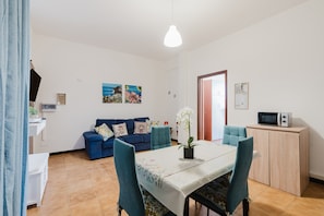Ein Wohnzimmer mit einer Couch, einem Esstisch mit Stühlen, einer Topfpflanze und einer Mikrowelle auf einem Schrank.