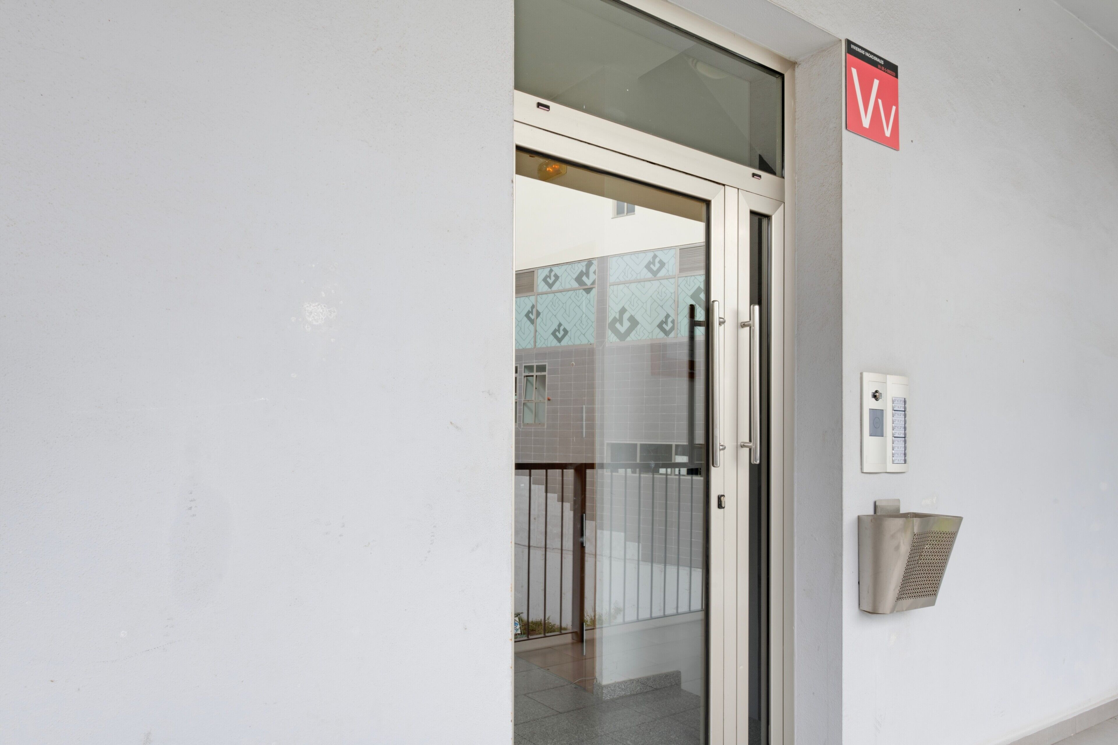 Une porte avec un panneau en verre, un portail en métal et un interphone fixé au mur.