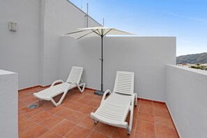 Un balcon avec deux fauteuils blancs et un seul parasol.