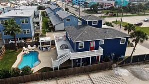 Un quartier résidentiel avec une maison bleue dotée d’une terrasse à l’avant, d’une piscine et d’une cour clôturée.