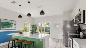 A modern kitchen with a central island, bar stools, pendant lighting, and a view to the outdoors.
