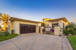 A residential house with a large garage door, a well-maintained front yard with plants, and a clear sky.