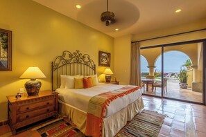 Camera d'albergo con un letto grande, due lampade ai comodini, un tavolino e un tappeto decorato, con vista sull'esterno tramite una porta scorrevole in vetro.