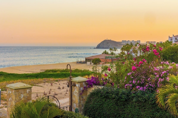 A coastal view with a beach, a stone gate, and a building with a red roof.