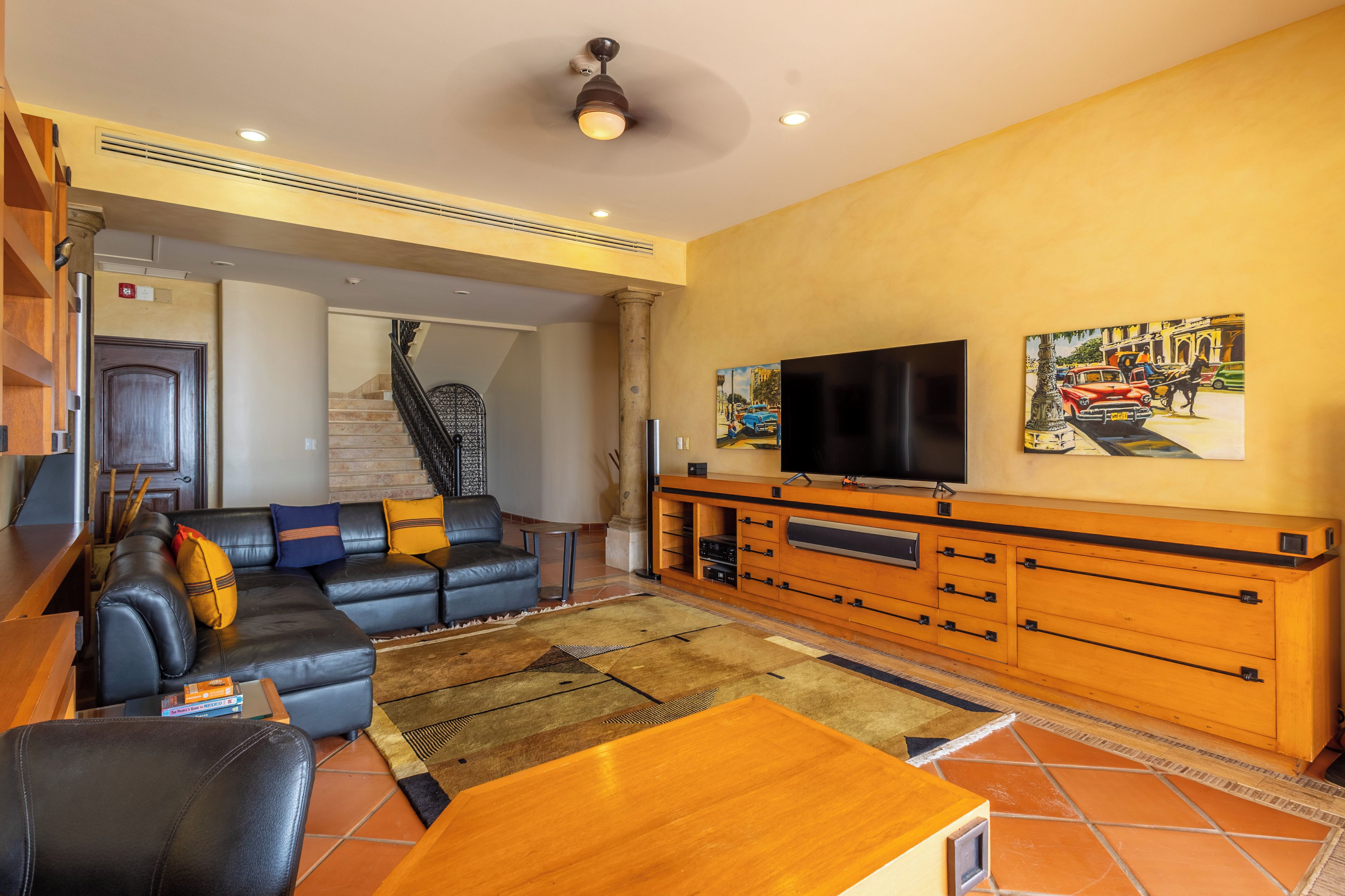 A living room with a sofa, TV, wooden cabinet, and a staircase leading to another room.