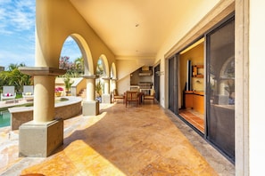A covered outdoor patio with a pool, a dining area, and a kitchen visible through a sliding door.