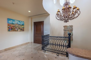 A hallway with a decorative iron railing, a stone wall, a wooden door, and a painting on the wall.
