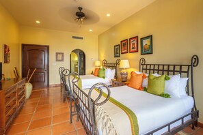 Une chambre d’hôtel avec deux lits, une commode en bois, un ventilateur de plafond et des tableaux encadrés accrochés au mur.