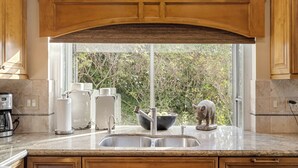 Une cuisine dotée d’une grande fenêtre, d’un évier à deux bacs, de meubles de rangement en bois et d’une statue d’éléphant décorative.