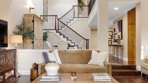 Un salon spacieux avec un canapé en cuir marron, une table basse en bois et un escalier menant à l’étage supérieur.