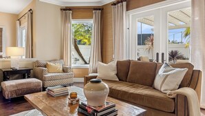 Un salon avec un canapé marron, une table basse avec des livres et un vase, un fauteuil à motifs et une fenêtre avec des rideaux.