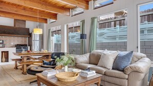 A cozy living room with a wooden ceiling, a beige sofa, a coffee table, and a dining area with a kitchen in the background. - California Dreamin by AvantStay | Private Pool + Fire Pit | Near the Beach (Carlsbad)