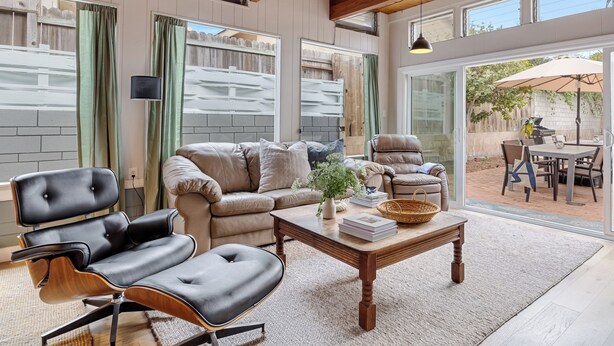 A spacious living room with a leather sofa, a wooden coffee table, and a view of an outdoor patio area. - California Dreamin by AvantStay | Private Pool + Fire Pit | Near the Beach (Carlsbad)