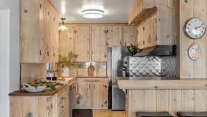 A kitchen with wooden cabinets, a stainless steel refrigerator, a sink, and a clock on the wall. - California Dreamin by AvantStay | Private Pool + Fire Pit | Near the Beach (Carlsbad)