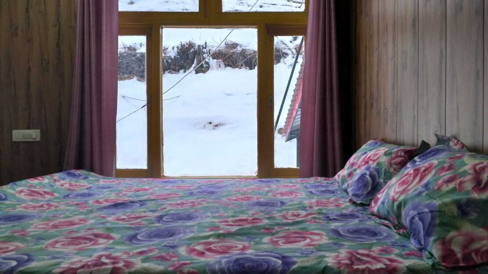 A bedroom with a bed, floral bedding, and a window with a view of a snowy landscape.
