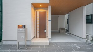 A modern building entrance with a wooden door, a utility box, and a covered area with a bench.