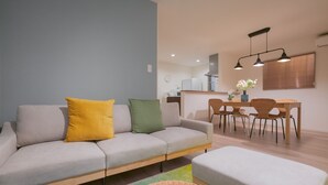 A modern living room with a grey sofa, a small table, and a dining area with wicker chairs.