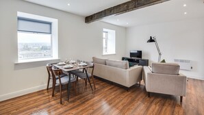 A modern living room with a dining table set for four, a sofa, and a TV. - Host Stay Canalside Lofts Apartment (Burnley)