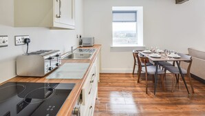 A modern kitchen with a built-in stove, a toaster, and a microwave. There is a dining area with a table set for four, and a window providing a view of the city. - Host Stay Canalside Lofts Apartment (Burnley)