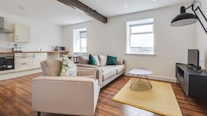 A modern living room with a sofa, a small round table, and a television. - Host Stay Canalside Lofts Apartment (Burnley)
