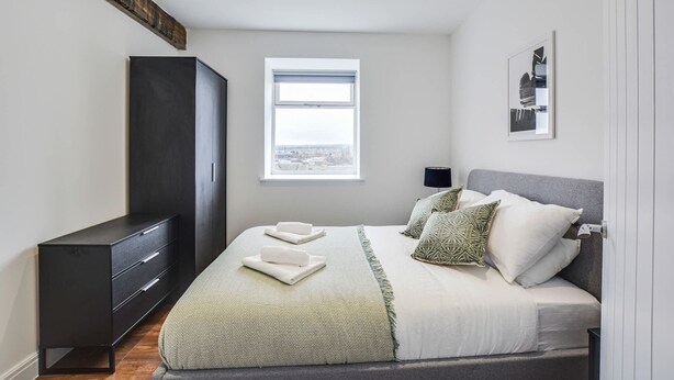 A bedroom with a large bed, a wardrobe, a window, and a city view. - Host Stay Canalside Lofts Apartment (Burnley)