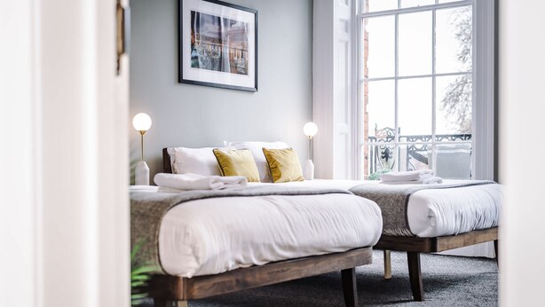 A bedroom with two beds, a framed picture on the wall, and a window with a view of the outside.