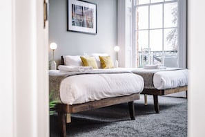A bedroom with two beds, a framed picture on the wall, and a window with a view of the outside. - Host Stay The Georgian Quarters at Canning III and IV (Liverpool)