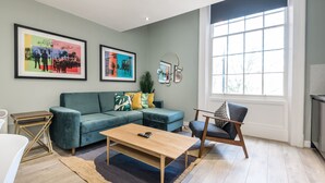 A living room with a teal sofa, a wooden coffee table, and a large window.