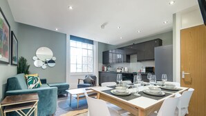 A modern living room with a sofa, a dining table set for four, and a kitchen in the background.