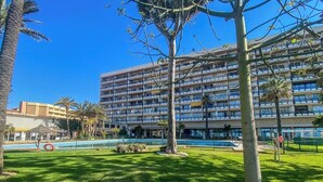 Et hotel med en stor bygning, en swimmingpool og en velplejet græsplæne med træer.