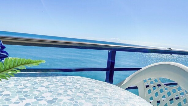 En balkon med fri udsigt over havet, et flisebelagt bord og en hvid stol.